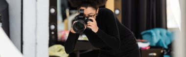 Siyah balıkçı yaka kazaklı Afro-Amerikan yapımcı fotoğraf stüdyosunda dijital kamerayla fotoğraf çekiyor.