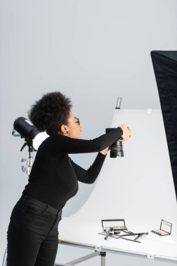 Afro-Amerikan içerik yöneticisi fotoğraf stüdyosundaki çekim masasında güzellik aletlerinin ve dekoratif kozmetik ürünlerin fotoğrafını çekiyor.