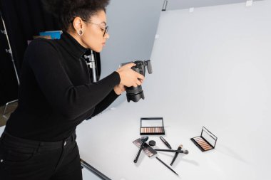 Afrikalı Amerikalı fotoğrafçı fotoğraf stüdyosunda dekoratif kozmetik ve güzellik aletlerinin fotoğrafını çekiyor.