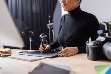 Fotoğraf stüdyosunda bilgisayar üzerinde çalışırken grafik tablet kullanan Afro-Amerikan rötuş görüntüsü.