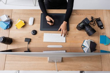 Afro-Amerikan rötuş cihazının dijital kamera ve fotoğraf stüdyosundaki renk örneklerinin yanında grafik tablet ve bilgisayar üzerinde çalışmasının en üst görüntüsü.