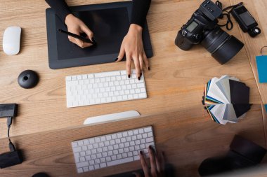 Renk örnekleri ve fotoğraf stüdyosundaki dijital kamera yanında grafik tablet ve klavye kullanan Afro-Amerikan rötuş cihazının en üst görüntüsü
