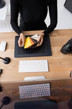 Afro-Amerikan rötuşçusunun fotoğraf stüdyosundaki fotoğraf stüdyosundaki fotoğraf makinesi ve grafik tablet yakınındaki renk örneklerini seçerken üst görüntüsü.
