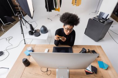 Modern fotoğraf stüdyosunda renkli örnekler ve grafik tablet yanında oturan Afro-Amerikan rötuş cihazının yüksek açılı görüntüsü