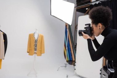 Fotoğraf stüdyosundaki son moda ceketin fotoğrafını çeken Afro-Amerikan içerik üreticisinin yan görüntüsü