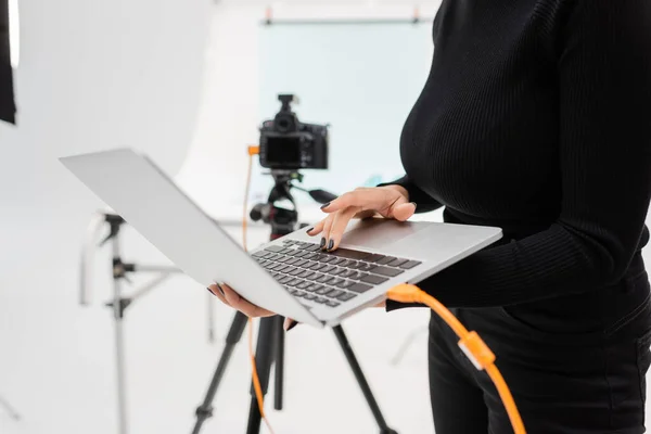 非洲裔美国内容经理在照片工作室用笔记本电脑在三脚架上接近模糊数码相机的剪影 — 图库照片