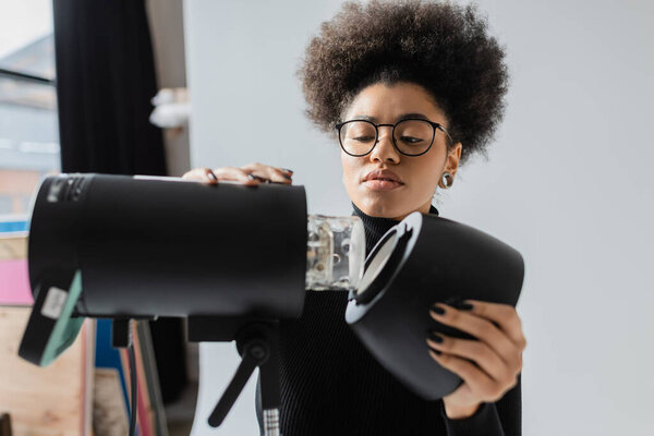 african american content maker in eyeglasses assembling strobe spotlight in photo studio