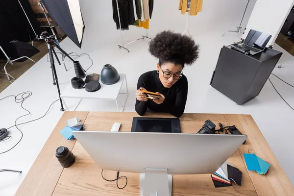 Modern fotoğraf stüdyosunda renkli örnekler ve grafik tablet yanında oturan Afro-Amerikan rötuş cihazının yüksek açılı görüntüsü