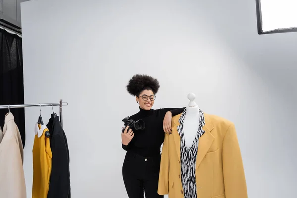 快乐的非洲内容制造者 带着数码相机 在摄影棚里穿着时髦外套 摆出一副近于人体模特的姿势 — 图库照片