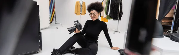 現代の写真スタジオに座ってデジタルカメラを持つ陽気なアフリカ系アメリカ人コンテンツ制作者バナー — ストック写真