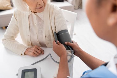 partial view of multiracial nurse measuring blood pressure of senior woman with grey hair  clipart