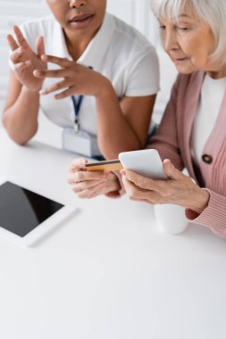 Çok ırklı sosyal hizmetler görevlisi kredi kartı ve akıllı telefonlu yaşlı kadına online alışveriş yapmayı anlatıyor. 