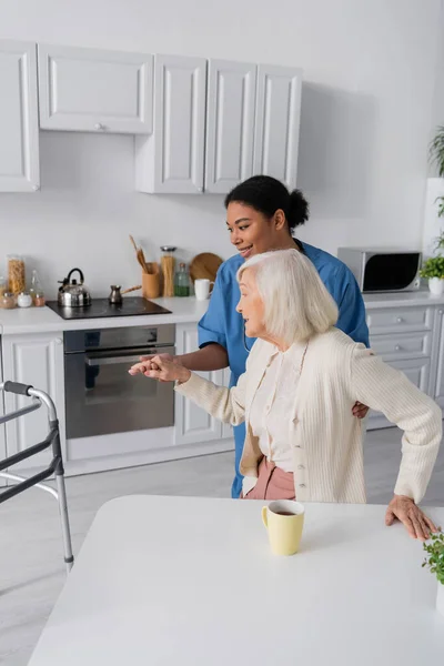 Happy Multiracial Caretaker Blue Uniform Holding Hand Senior Woman Grey — Stock Photo, Image