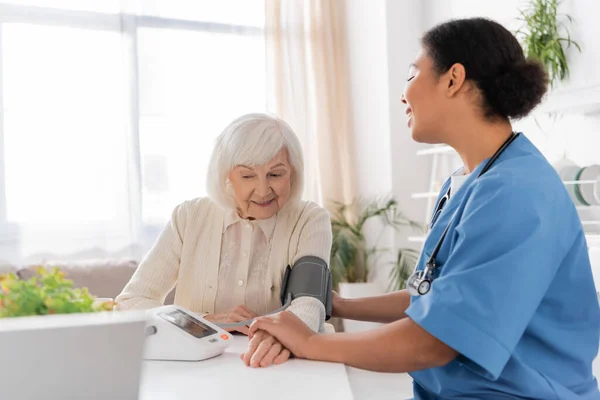 Radosna Pielęgniarka Wielorasowa Mierząca Ciśnienie Krwi Starszej Kobiety Siwymi Włosami — Zdjęcie stockowe