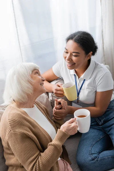 快乐的多种族社工一边在客厅喝茶 一边和年长女人聊天 — 图库照片