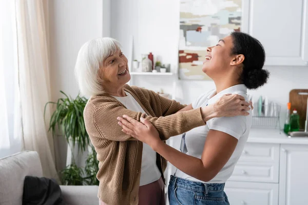 Pozytywny Wielorasowy Pracownik Socjalny Starsza Kobieta Śmieją Się Przytulają Salonie — Zdjęcie stockowe
