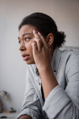 Disappointed multiracial woman with depression looking away at home  clipart