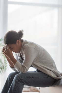 Depresyondaki çok ırklı kadın evde yatakta otururken kafasına dokunuyor. 