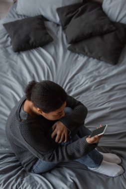 Yatakta akıllı telefon tutan, depresyonlu, çok ırklı bir kadın. 