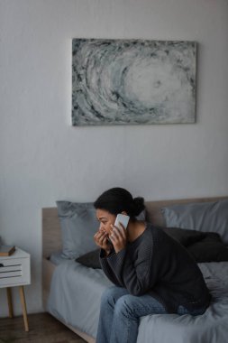 Yatak odasında yatakta akıllı telefondan konuşan çok ırklı bir kadın. 