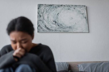 Yatak odasında depresyonlu, bulanık, çok ırklı bir kadının yanındaki duvarda resim. 