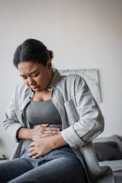 Upset multiracial woman having abdomen pain on bed at home 