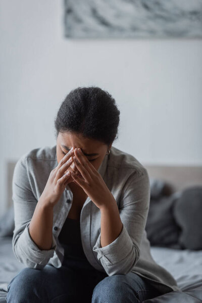 Depressed multiracial woman crying on blurred bed at home 