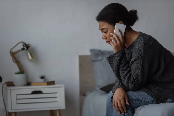 Πληγωμένη Πολυφυλετική Γυναίκα Πουλόβερ Που Μιλάει Στο Smartphone Στο Κρεβάτι — Φωτογραφία Αρχείου