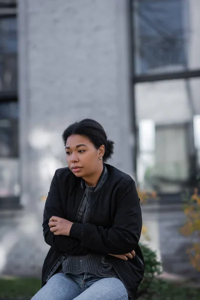 stock image Frustrated multiracial woman in jacket sitting on bench on urban street 