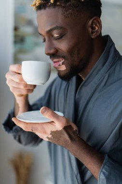 Neşeli Afrikalı Amerikalı Vitiligo 'lu adam elinde bir fincan kahve tutuyor. 