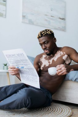 Vitiligo 'lu kaslı Afrikalı Amerikalı adam elinde kahve, yatak odasında gazete okuyor. 