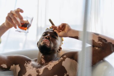 Evde banyo yaparken elinde puro ve bir bardak viski tutan Afrikalı Amerikalı bir adam. 