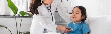 Steteskoplu doktor Pediyatri Hastanesi 'nde neşeli Asyalı kızı muayene ediyor.