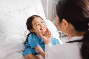 Hastane koğuşunda dil bastırıcılı bulanık doktora dişlerini gösteren küçük Asyalı kız.