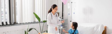 Modern pediatri kliniğinde elinde balonla gezen mutlu Asyalı doktor.