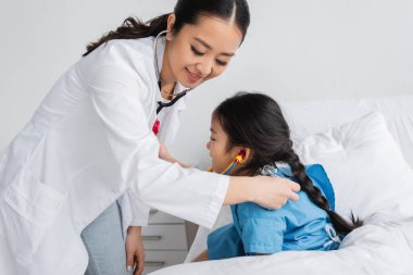 Steteskoplu pozitif Asyalı doktor pediatri kliniğinde küçük bir hastayı muayene ediyor.