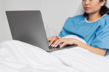 Hastane koğuşunda laptopta yazı yazan Asyalı kadının kısmi görüntüsü