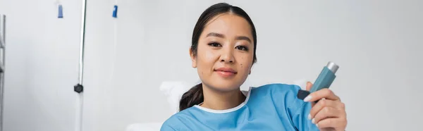 高兴的亚洲女人拿着吸入器 看着诊所里的相机 — 图库照片