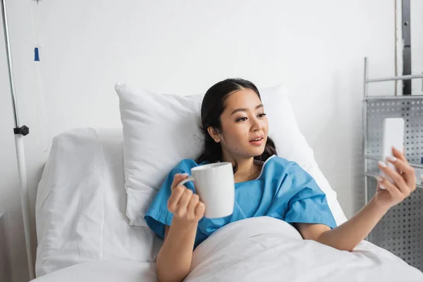Surprised Asian Woman Cup Tea Looking Mobile Phone Hospital Ward — Stock Photo, Image