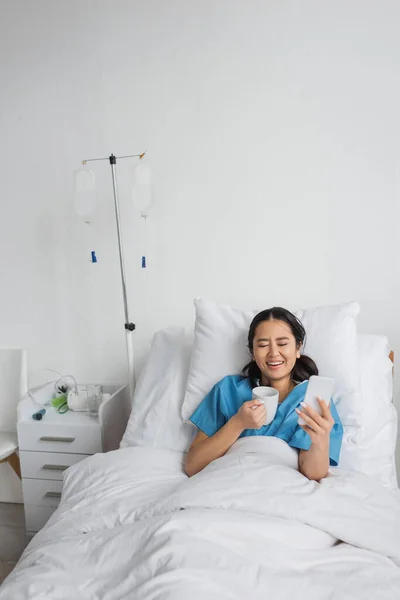 Excited Asian Woman Smartphone Cup Tea Laughing Closed Eyes Hospital — Stock Photo, Image