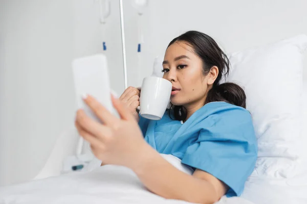 Young Asian Woman Drinking Tea Looking Blurred Cellphone Hospital Ward — Stock Photo, Image
