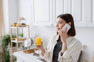 Akıllı telefondan konuşan ve elinde portakal suyu tutan genç bir kadın. 