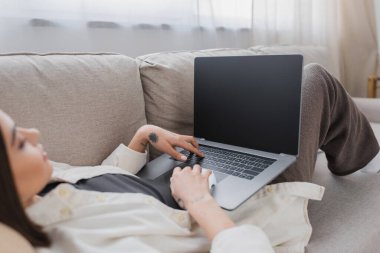Bulanık dövmeli serbest çalışan evdeki koltukta boş ekranlı dizüstü bilgisayar kullanıyor. 