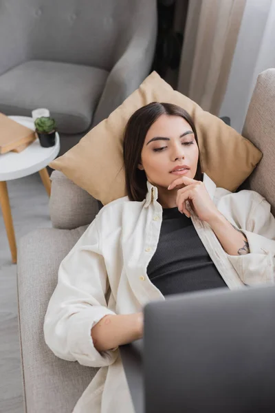 Young Tattooed Freelancer Using Blurred Laptop While Lying Couch Home — Stock Photo, Image