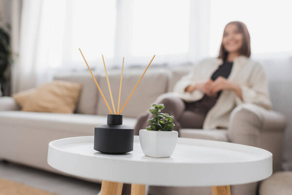 Bamboo aroma sticks and plant on coffee table near blurred woman at home 