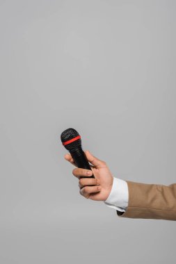 Cropped view of young event host in blue jacket and white shirt holding wireless microphone while standing isolated on grey with copy space  clipart