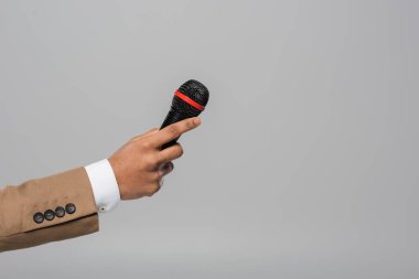 Gri üzerinde tek başına dururken, performans sırasında mikrofon tutan kahverengi ceketli ev sahibinin kırpılmış görüntüsü  