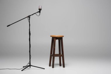 Kahverengi ahşap sandalye mikrofonun yanında duruyor gri arka planda fotokopi alanı ve stüdyoda yüksek tabure var. 