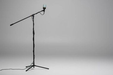 Black microphone with wire on metal stand on grey background with copy space  clipart