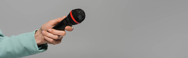 Cropped view of hand of event host in green jacket holding black wireless microphone during party isolated on grey with copy space, banner 